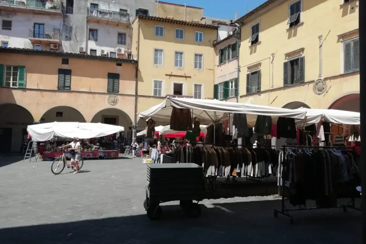 Mercato all'aperto nella piazza delle vettovaglie, con bancarelle di abbigliamento e persone che passeggiano.
