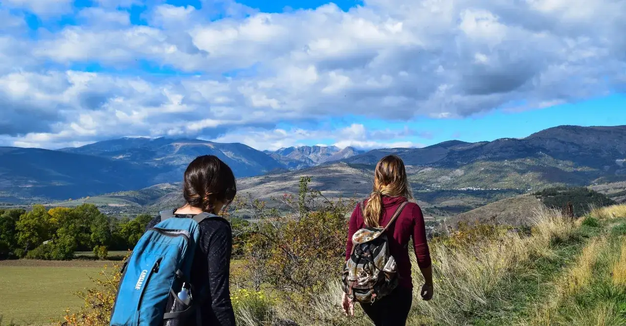 Due escursioniste con zaini ammirano un vasto paesaggio montano, un'immagine che evoca il cammino di San Jacopo.