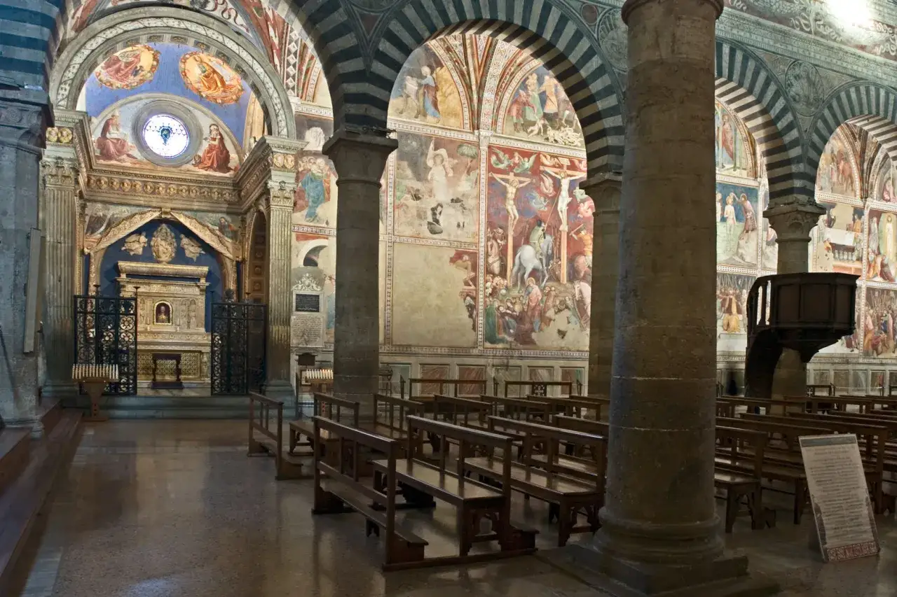 Interno del duomo di San Gimignano con affreschi medievali e panche di legno.