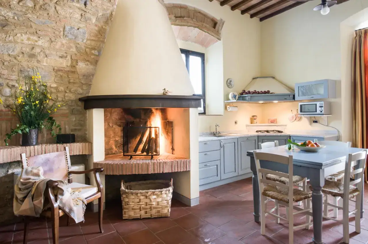 Accogliente cucina rustica con camino acceso, mobili grigi e un tavolo pronto per la colazione alla fattoria La Striscia.