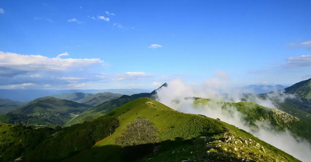 Vette verdi e nebbiolina avvolgono il monte Matanna, sotto un cielo azzurro con nuvole sparse.