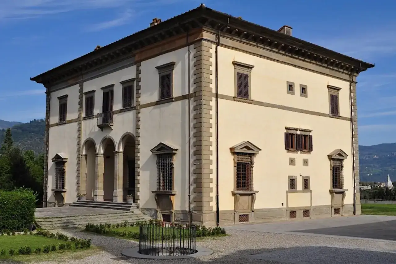 Villa Poggio Reale a Rufina, un'imponente dimora storica con un portico ad archi e finestre ornate, immersa nel verde della campagna toscana.