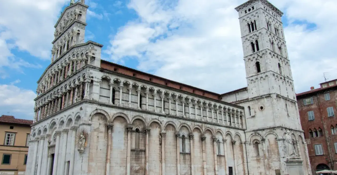 La splendida facciata e il campanile della chiesa di San Michele in Foro, in piazza San Michele Lucca, sotto un cielo azzurro con nuvole bianche.