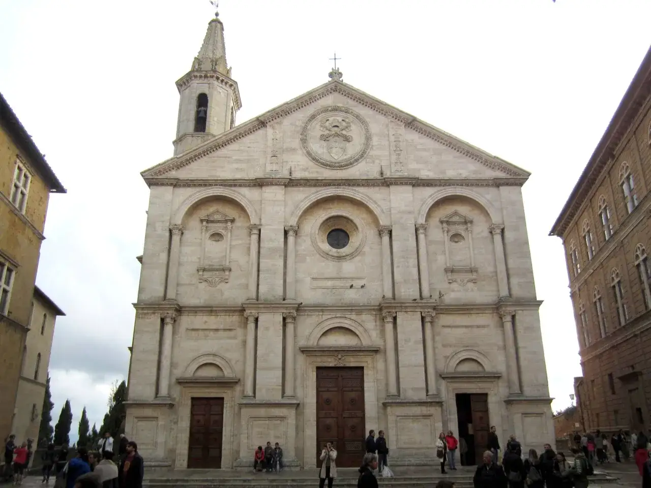 Il duomo di Pienza, con la sua facciata imponente e il campanile slanciato, domina la piazza. Turisti passeggiano e ammirano la bellezza rinascimentale.
