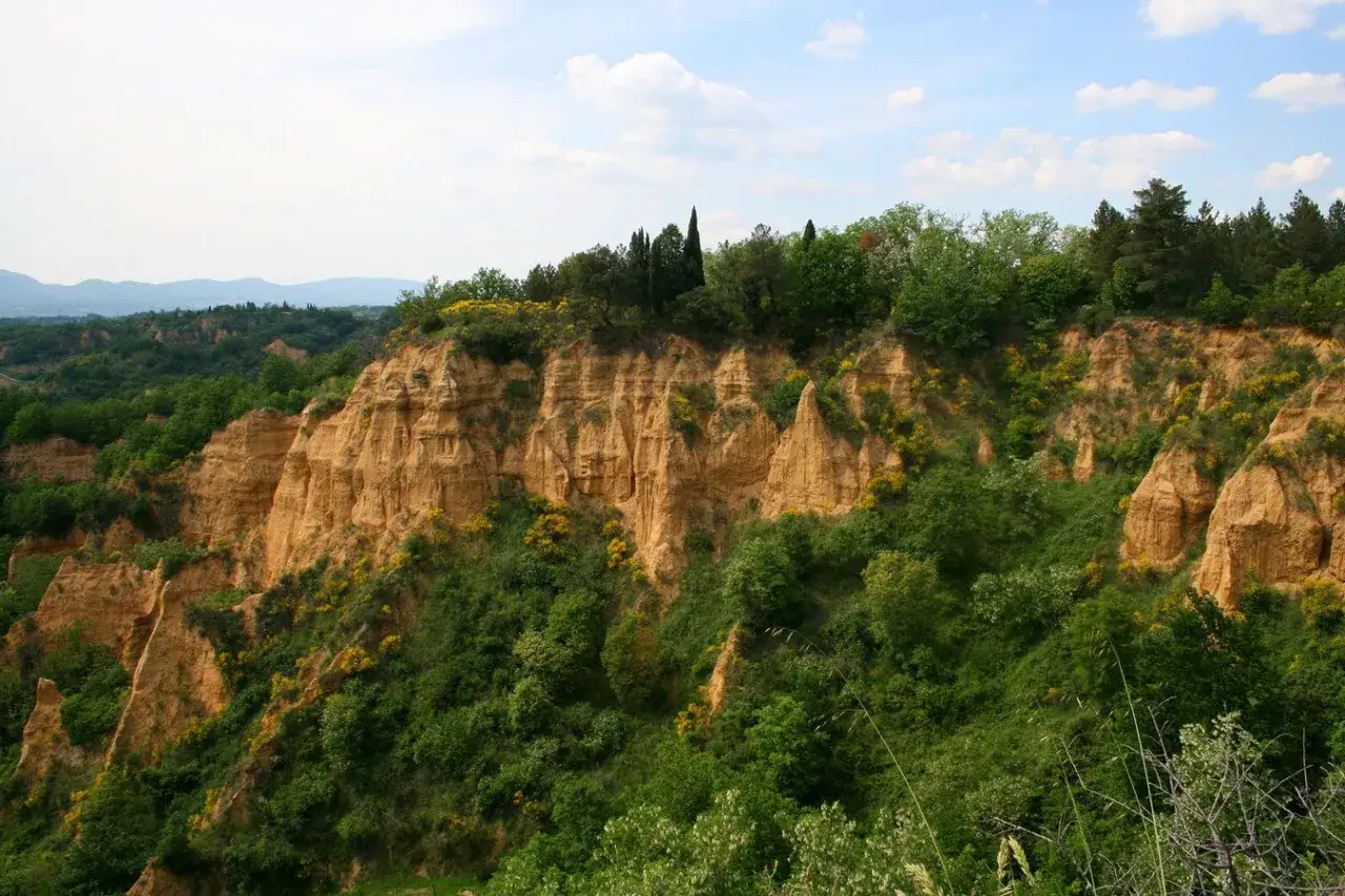 Le suggestive balze del Valdarno, con le loro formazioni argillose erose dal tempo, si ergono tra la vegetazione rigogliosa e il cielo azzurro.