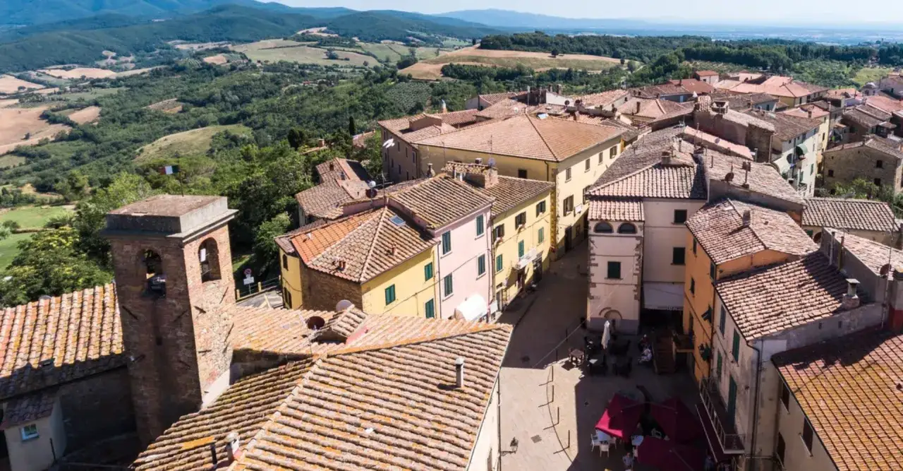 Vista aerea di un borgo toscano con tetti in cotto e una torre campanaria. Si intravede il paesaggio collinare di Castagneto Carducci.
