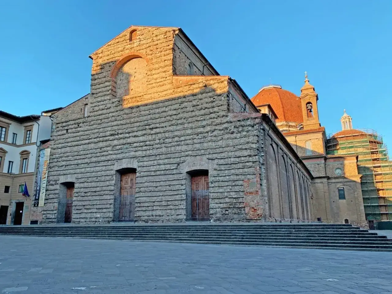 La facciata in pietra di San Lorenzo a Firenze, con la cupola arancione che domina il cielo azzurro.