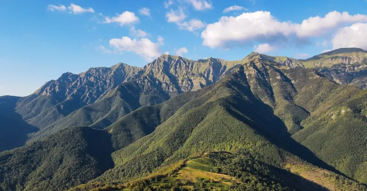 Viste panoramiche del passo del giogo, con montagne verdi e rocciose sotto un cielo azzurro con nuvole bianche.
