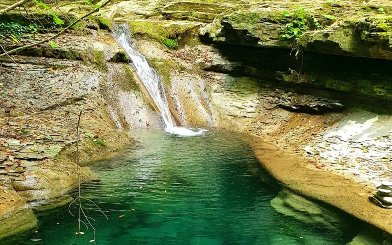 Cascata e pozza d'acqua cristallina tra rocce e vegetazione, un angolo segreto di Badia Tedalda.