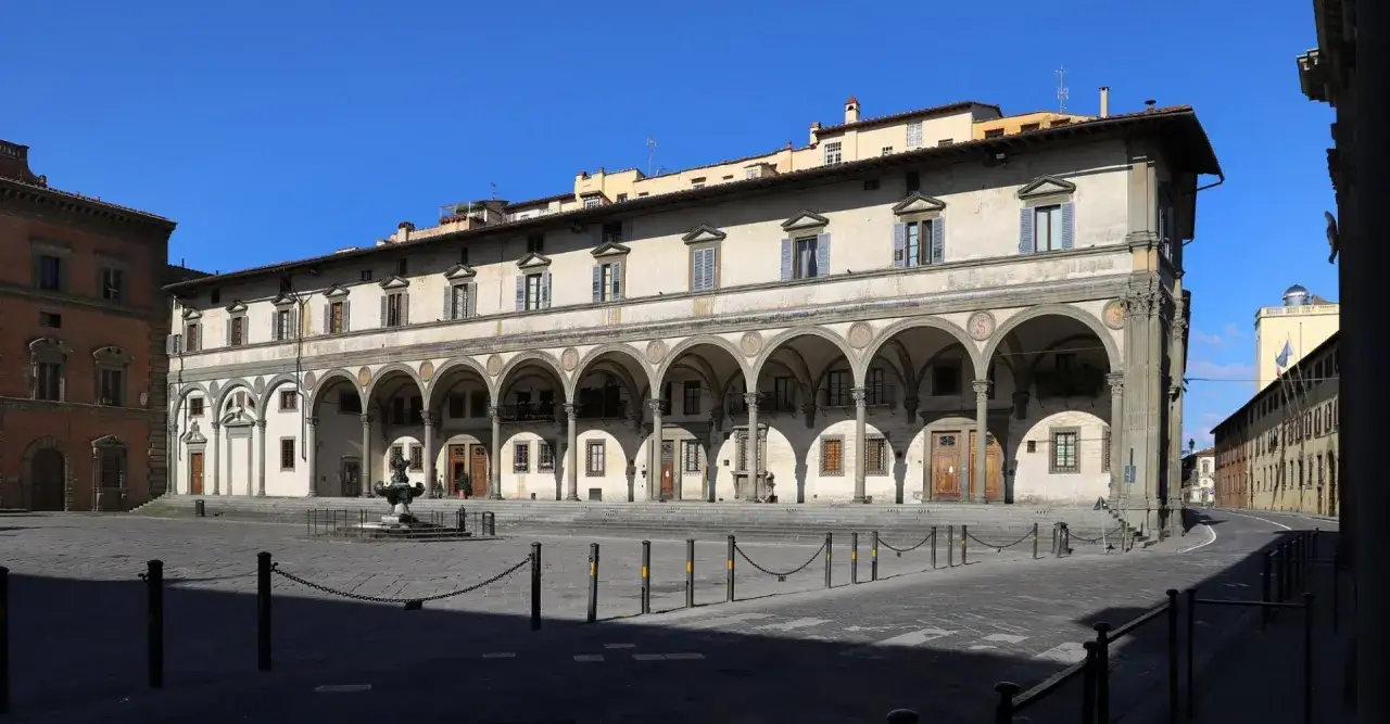 La piazza della Santissima Annunziata a Firenze, con il suo portico rinascimentale e la fontana centrale, sotto un cielo azzurro.