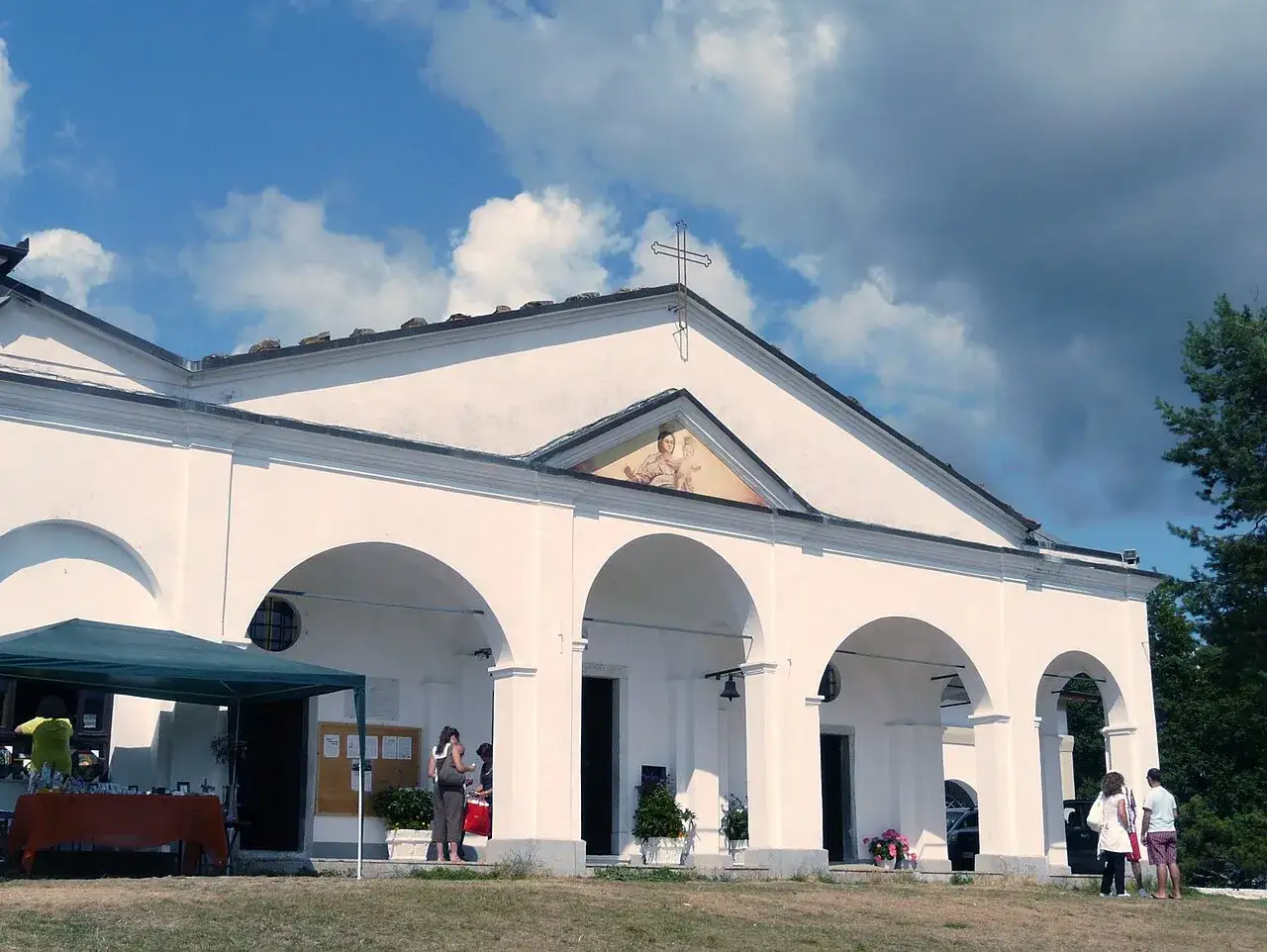 Chiesa bianca con portico ad archi sul monte Argegna, cielo azzurro con nuvole.