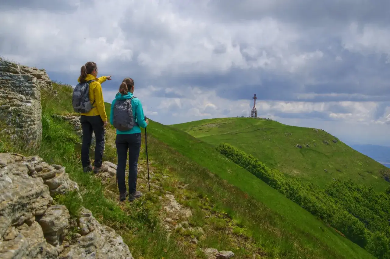 Due escursioniste ammirano il panorama del Pratomagno, Arezzo, con una croce in lontananza.