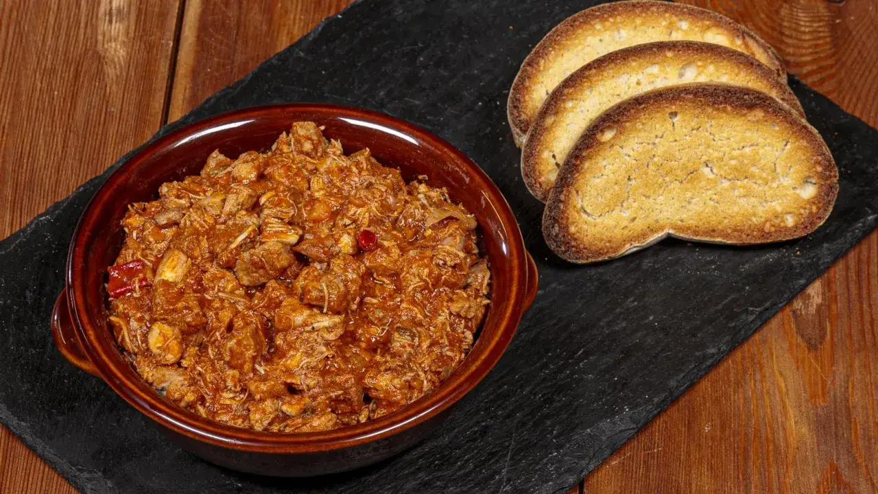 La scottiglia, un saporito stufato di carne in umido, servita in una ciotola di terracotta con fette di pane tostato.