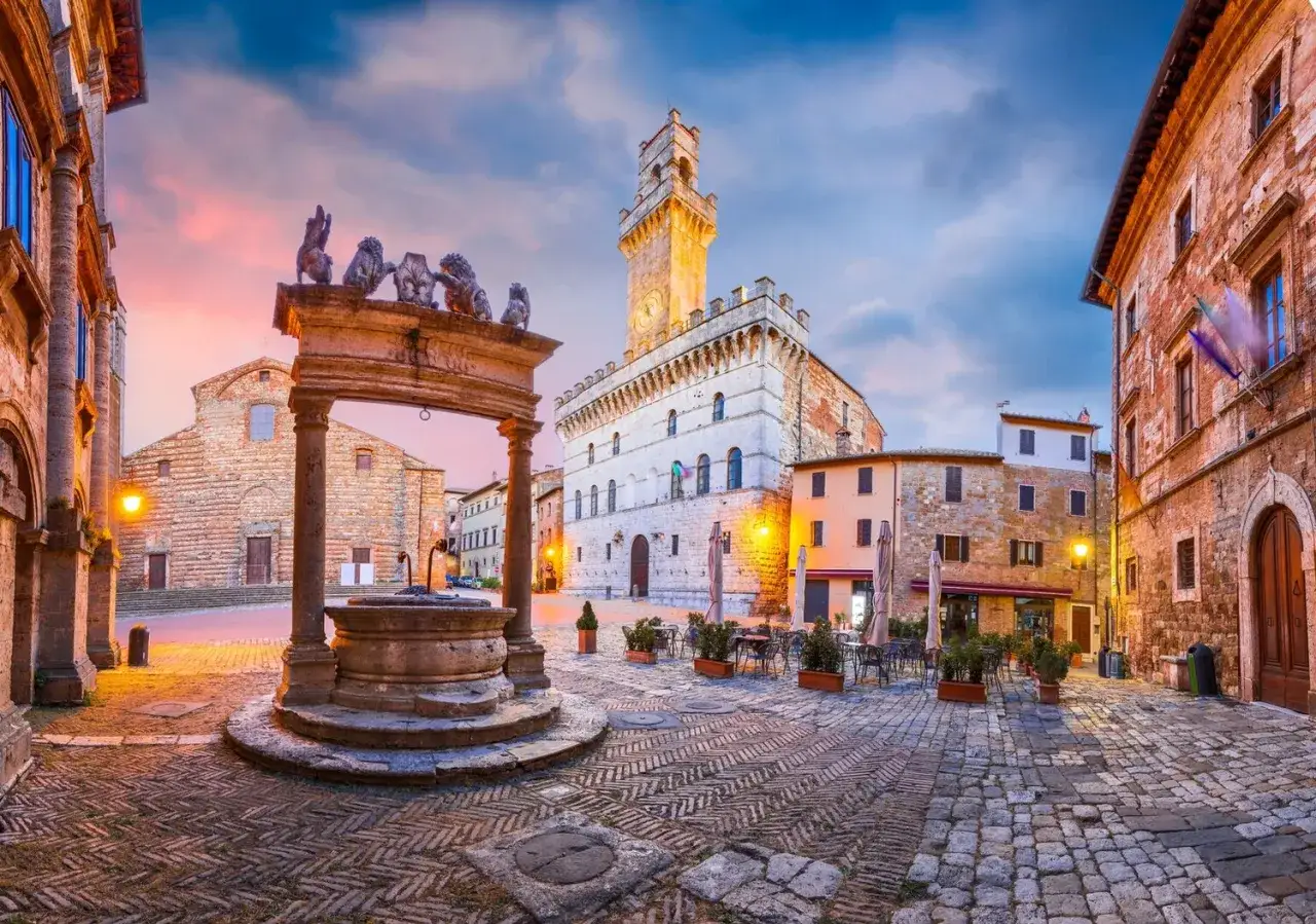 Piazza del Popolo a Montepulciano, un gioiello per cosa vedere ad Arezzo e dintorni in due giorni. Fontana, palazzi storici e un cielo al tramonto.