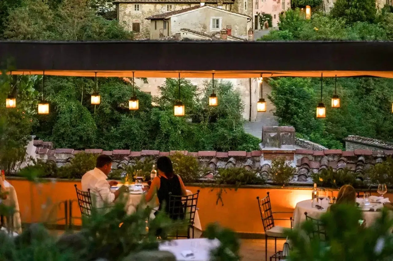 Coppia cena romantica in terrazza a Tenuta Il Borro, con lanterne soffuse e vista sul borgo toscano.