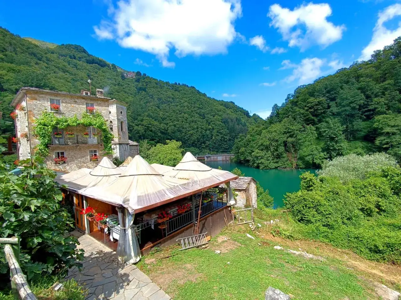 Un antico edificio in pietra con balconi fioriti domina un lago verde smeraldo. Un ristorante all'aperto invita a scoprire Careggine cosa vedere.