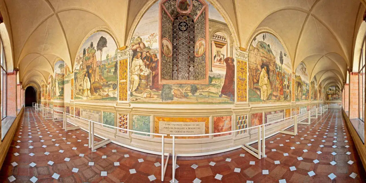 Corridoio affrescato a Monte Oliveto Maggiore, con scene di vita monastica e iscrizioni. Pavimento a losanghe rosse e bianche.