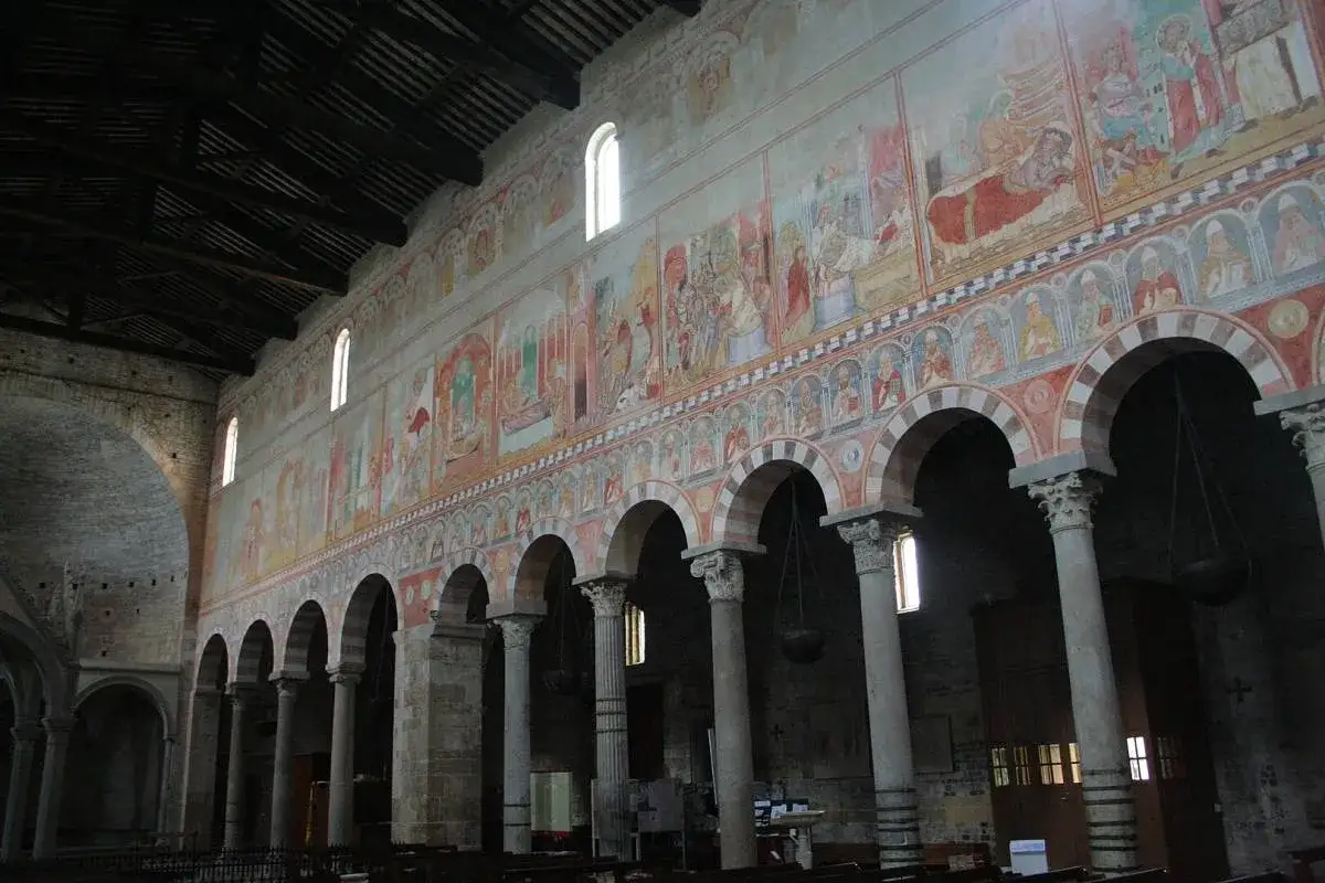 Interno della Basilica di San Piero a Grado con affreschi medievali che narrano storie sacre, colonne imponenti e archi a tutto sesto.