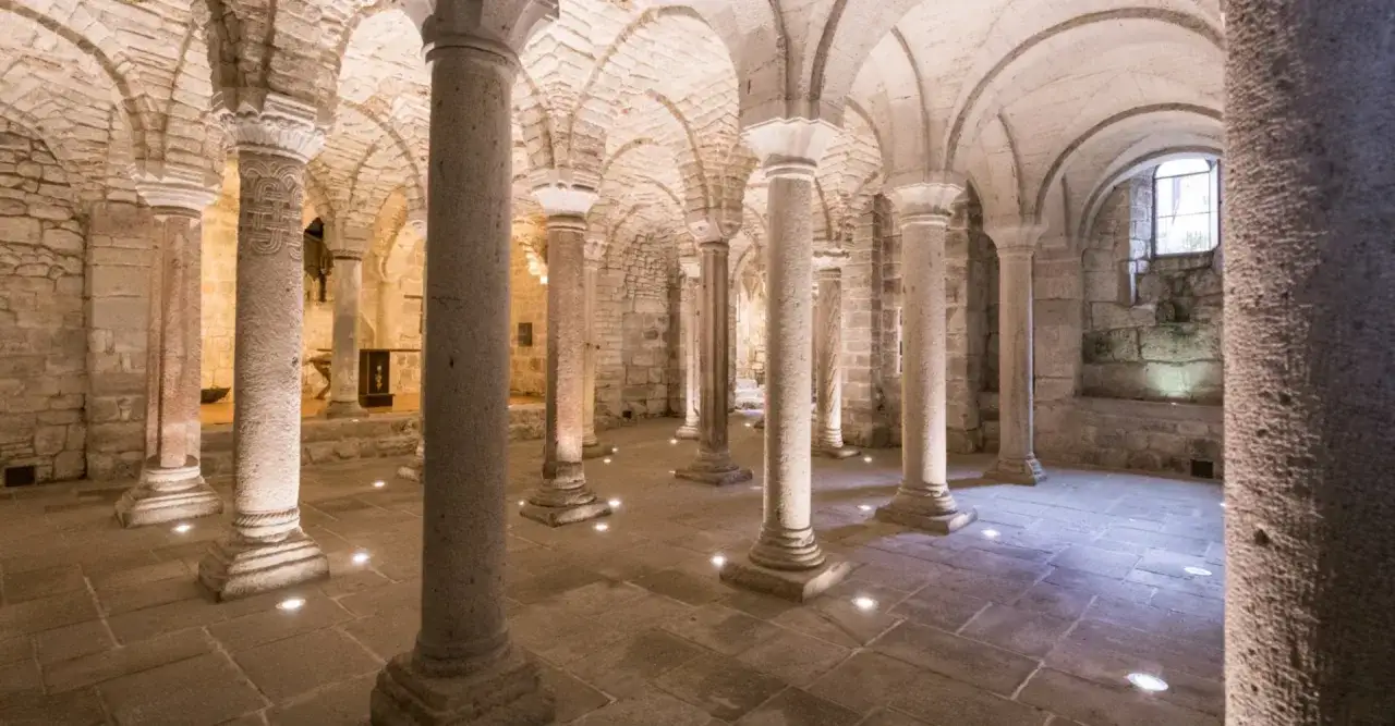 Cripta romanica dell'Abbazia di San Salvatore sul Monte Amiata, con colonne in pietra e soffitto a volta illuminato da faretti.
