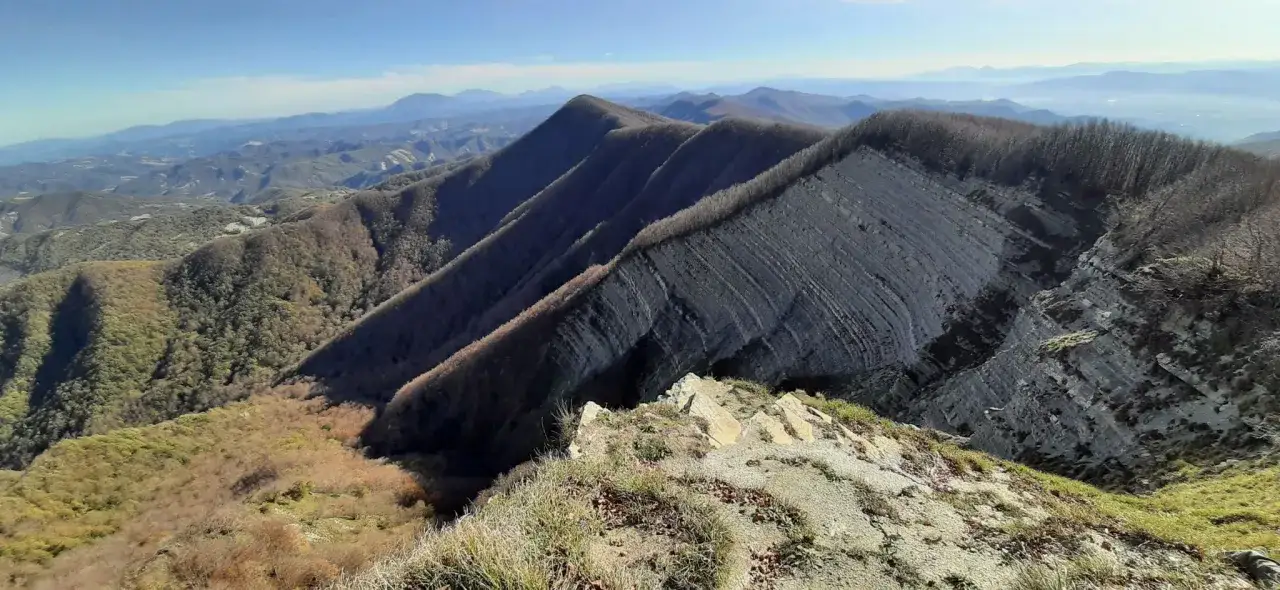Cime frastagliate e stratificate sull'Alpe della Luna, con boschi spogli e un cielo azzurro limpido.