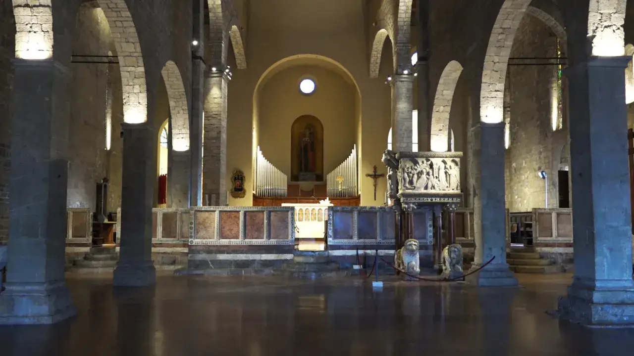 Interno di una chiesa romanica a Barga, Lucca, con colonne in pietra, un organo e un altare decorato.
