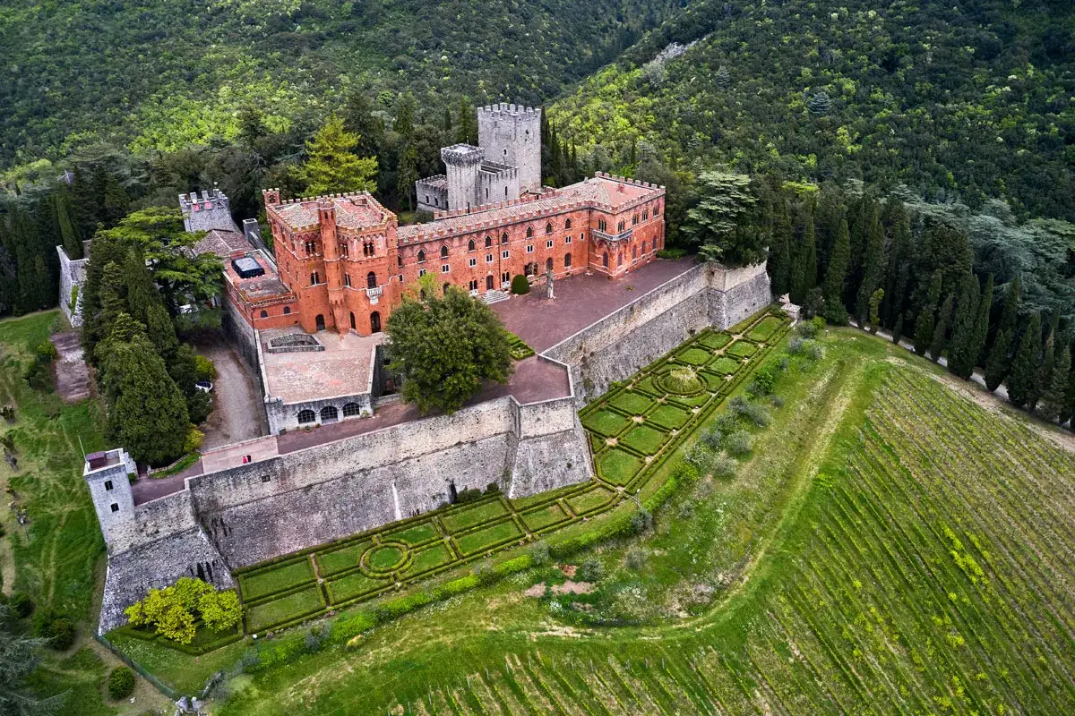 Il castello di Brolio, imponente fortezza in mattoni rossi, domina un paesaggio collinare con giardini all'italiana e vigneti rigogliosi.
