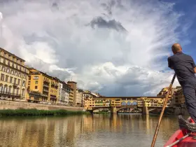 Un uomo su una barca a remi naviga lungo l'Arno, ammirando Ponte Vecchio e gli edifici storici di Firenze.