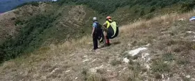 Due parapendisti si preparano al decollo sulla **Valle del Serchio**, con un paesaggio verdeggiante alle spalle.