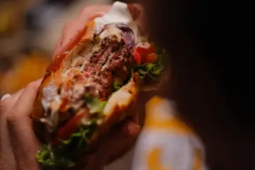 Mani che stringono un succulento hamburger, un'esplosione di sapori tipica dello street food ad Arezzo.