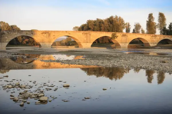 Ponte romanico con archi a tutto sesto, riflesso sull'acqua calma. I Setteponti di Arezzo, un'antica via, abbraccia la campagna toscana.