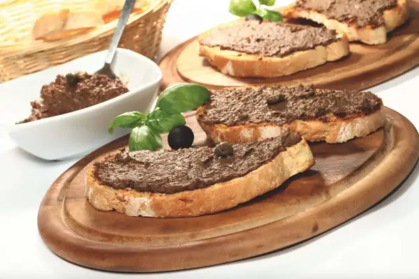 Toasted bread slices topped with dark spread, garnished with basil, olives, and capers.