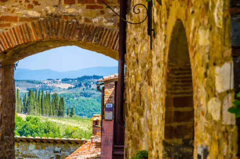 Arco in pietra che incornicia un panorama collinare toscano, con cipressi e vigneti, tipico dei borghi del Chianti.