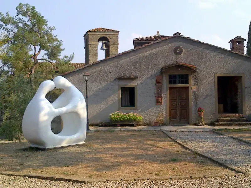 Scultura moderna di due figure abbracciate, simbolo di romena accoglienza, davanti a un edificio con campanile.