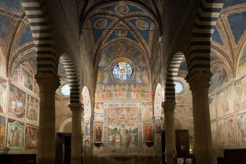 Interno del duomo di San Gimignano, con affreschi medievali che narrano storie sacre, volte a crociera a strisce bianche e nere e un rosone colorato.