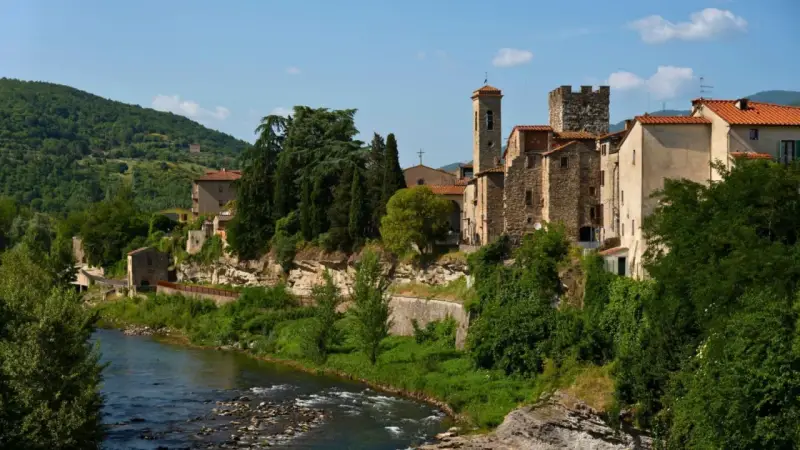 Borgo medievale di Subbiano, Arezzo, con il fiume che scorre ai suoi piedi e il verde rigoglioso che abbraccia le antiche pietre.